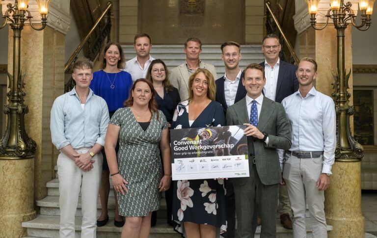 Wethouder Versnel met coalitiepartners en ondertekend bord op trap in het stadhuis van Rotterdam