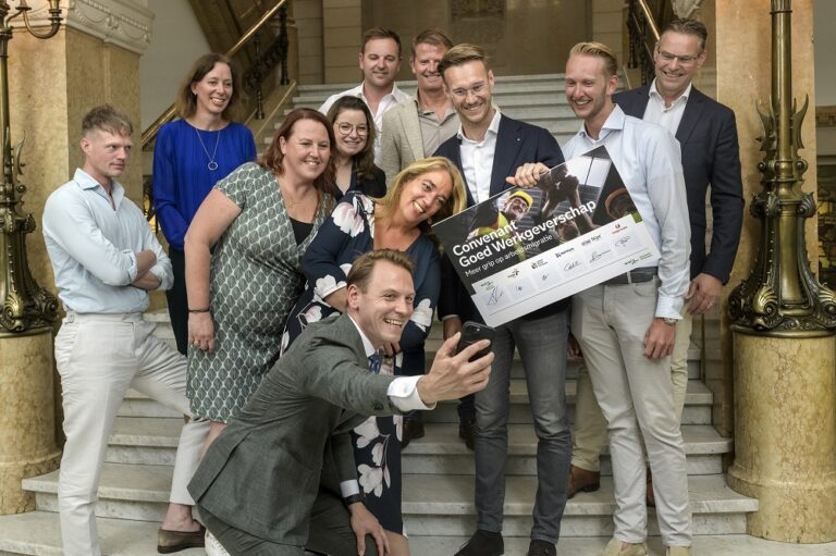 Wethouder Versnel maakt selfie met coalitiepartners en ondertekend bord op trap in het stadhuis van Rotterdam