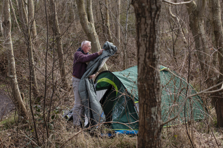 Dakloze man slaat tent op in begroeiing.
